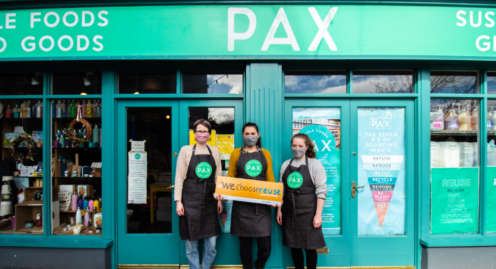 Employees of PAX standing outside the shop holding a "we choose reuse" banner